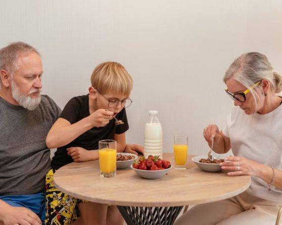 A family of three enjoying breakfast around a wooden table at home.